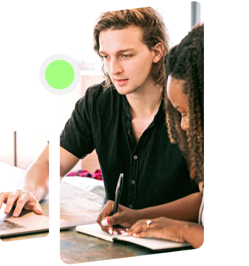 People collaborating with one working on a laptop and the other writing down notes in a notebook.