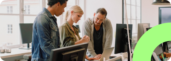 Three people collaborating at a table, looking at a laptop.