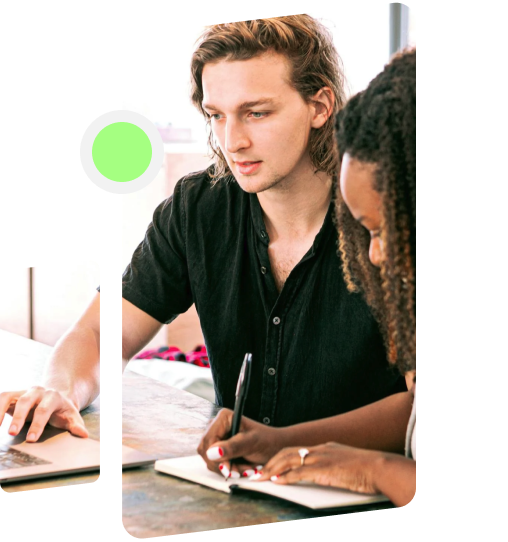 People collaborating with one working on a laptop and the other writing down notes in a notebook.